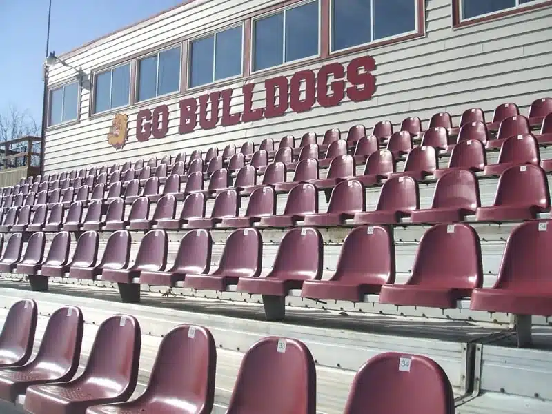 Rows of maroon stadium seats installed on bleacher supports below a Go Bulldogs press box