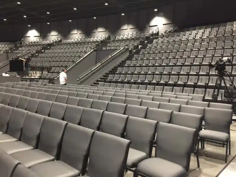 Gray upholstered chairs and fixed seating arranged across the iTown Church worship auditorium Gray upholstered chairs and fixed seating arranged across the iTown Church worship auditorium