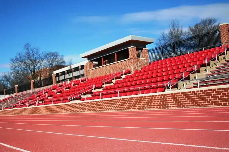 Rows of red stadium seats on concrete risers beside a track at an outdoor athletic venue