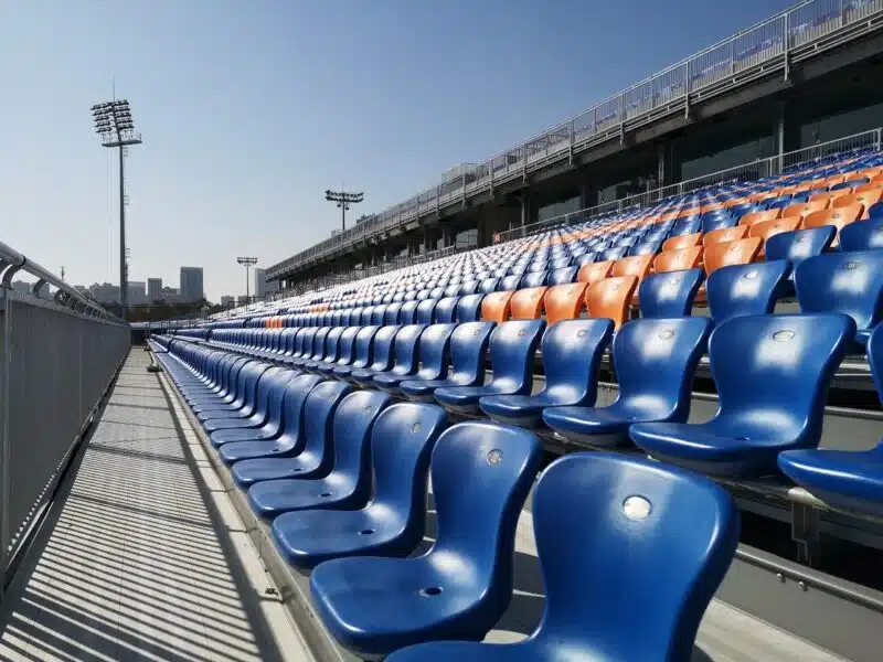 Rows of blue and orange molded plastic stadium seats installed on outdoor metal bleachers