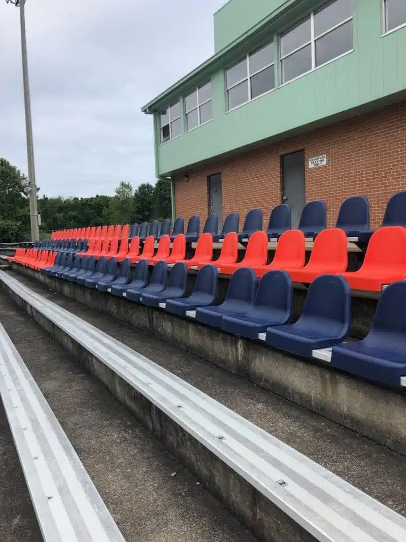 Orange and navy individual stadium seats installed on aluminum bleachers at a school stadium